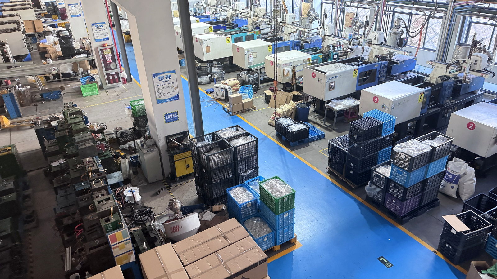 注塑车间全貌：成排生产设备、在制工件与蓝色通道上分区码放的物料周转箱